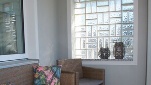 A wicker sofa with cushions, a glass-top coffee table, and a window with decorative items. - Fichtelherz Herzerl (barrier-free) - 89 m² - 2 bedrooms - balcony - max. 5 pers. (Thierstein)