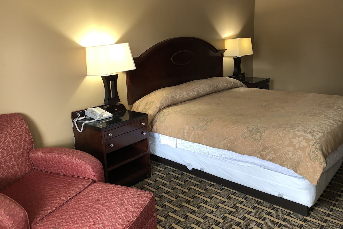 A hotel room with a bed, two bedside lamps, a telephone, a nightstand, and a red armchair.
