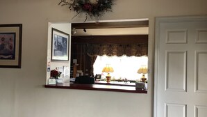 A reception area with a desk, a framed picture, a wall-mounted wreath, and a door. - Caronoda Motel (Central City)