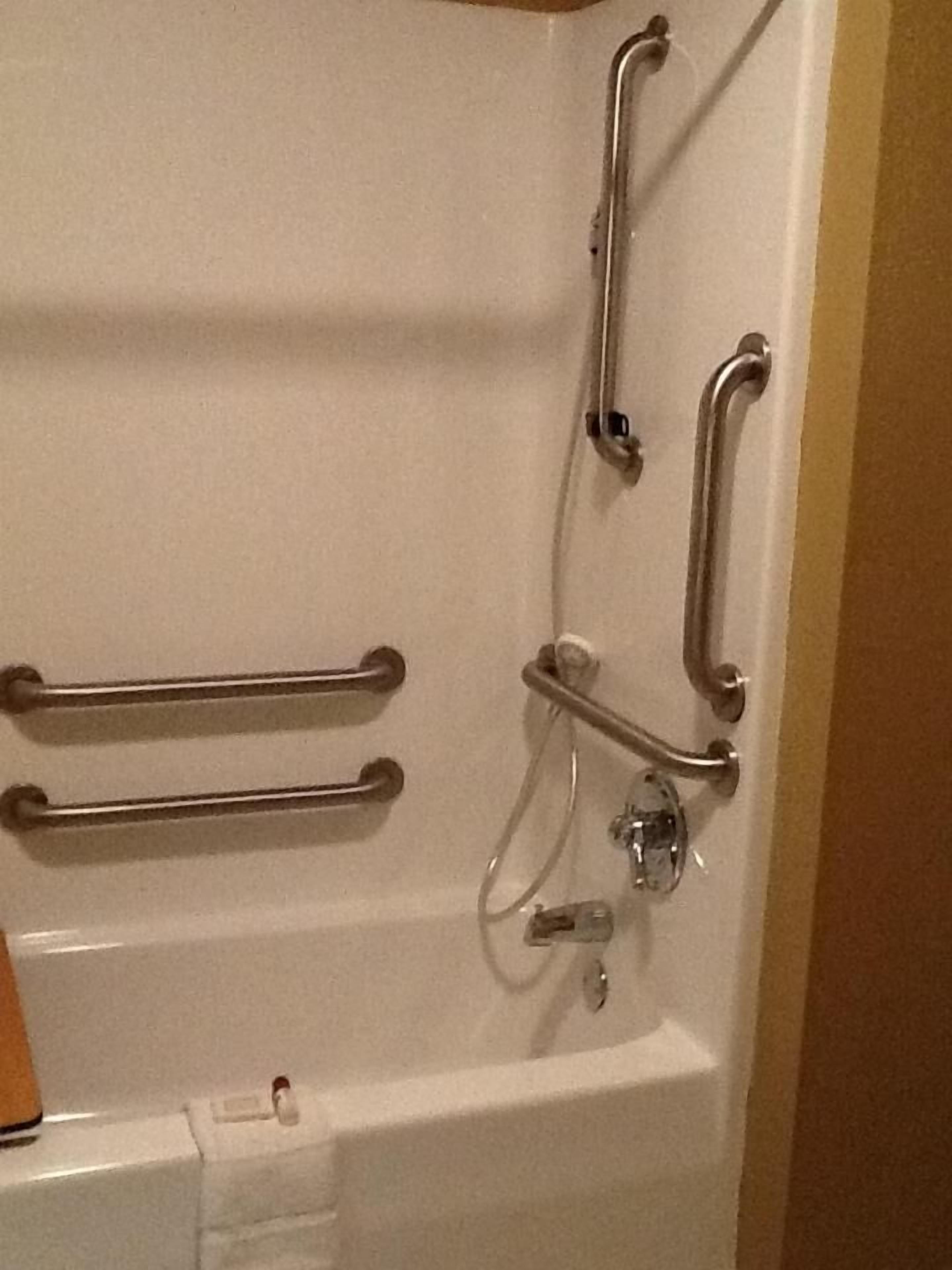A bathroom with a white bathtub, grab bars, and a shower control panel.