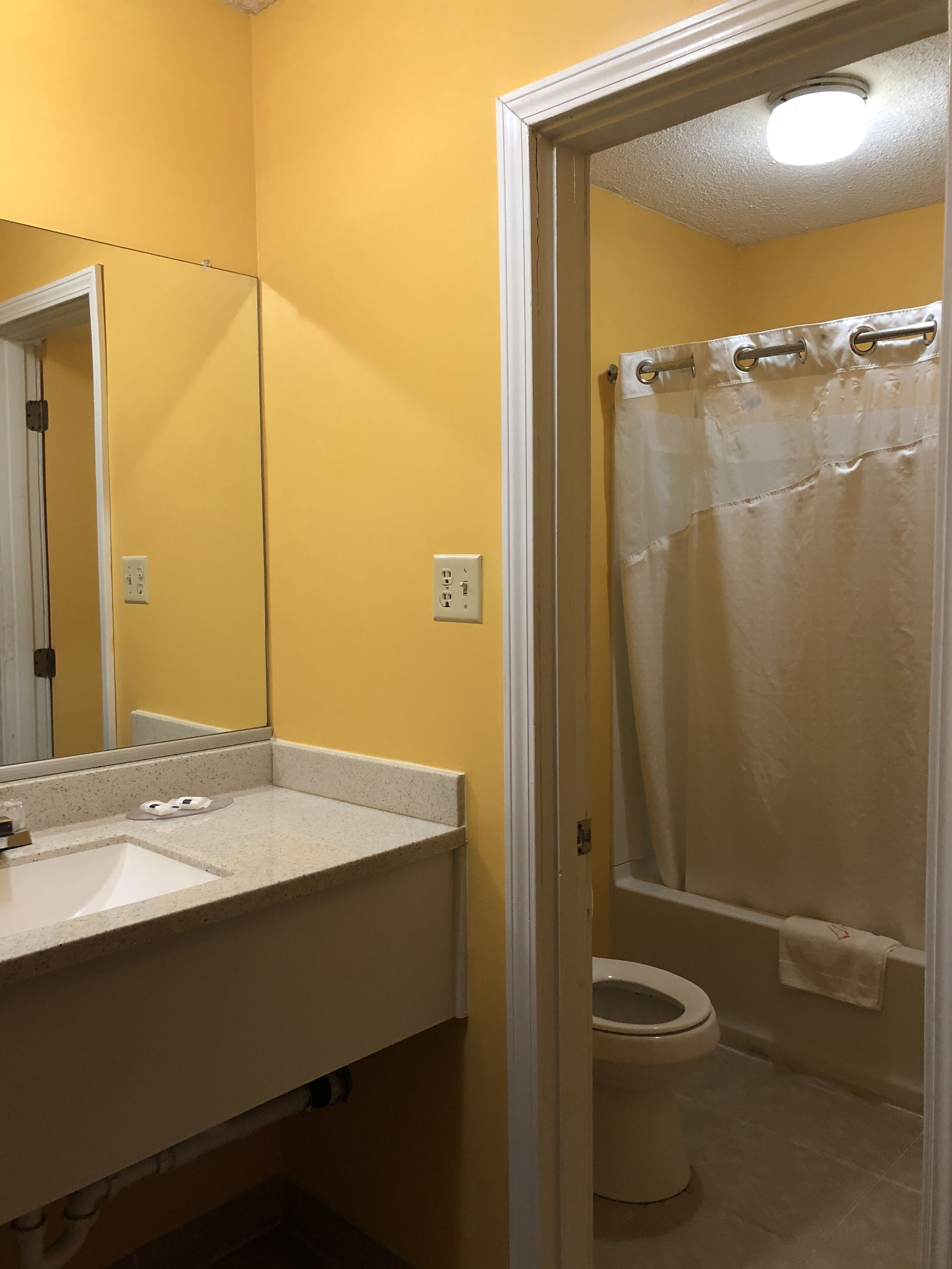 A bathroom with a yellow wall, a white sink, a mirror, and a shower curtain.
