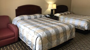 A hotel room with two beds, a nightstand with a lamp, and a red armchair. - Caronoda Motel (Central City)