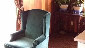 A room with a blue armchair, wooden walls, a red patterned carpet, and two potted plants on a wooden table. - Caronoda Motel (Central City)