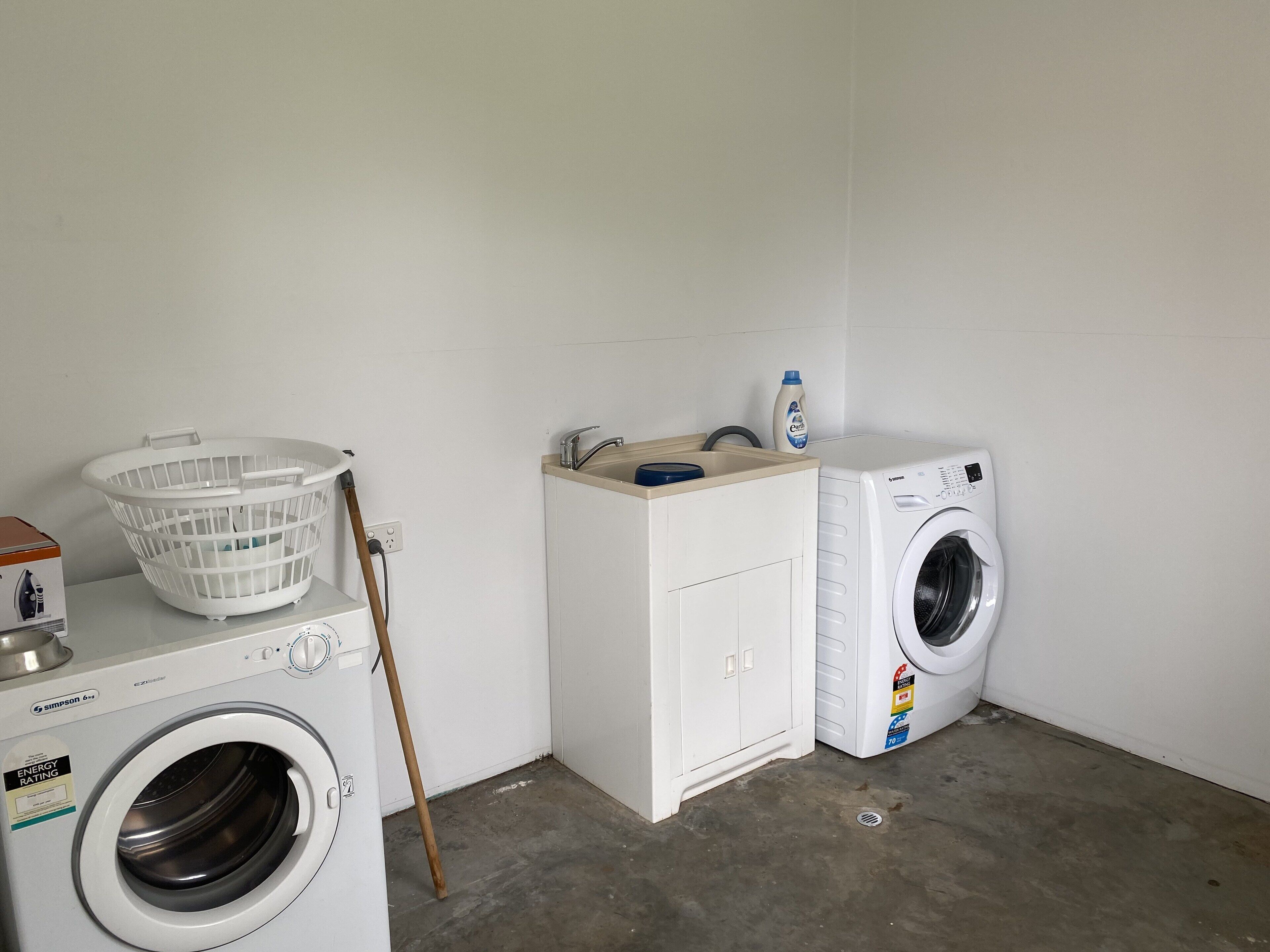 Un espacio para lavandería con lavadora, secadora, un armario blanco, una cesta de ropa y una botella de detergente.