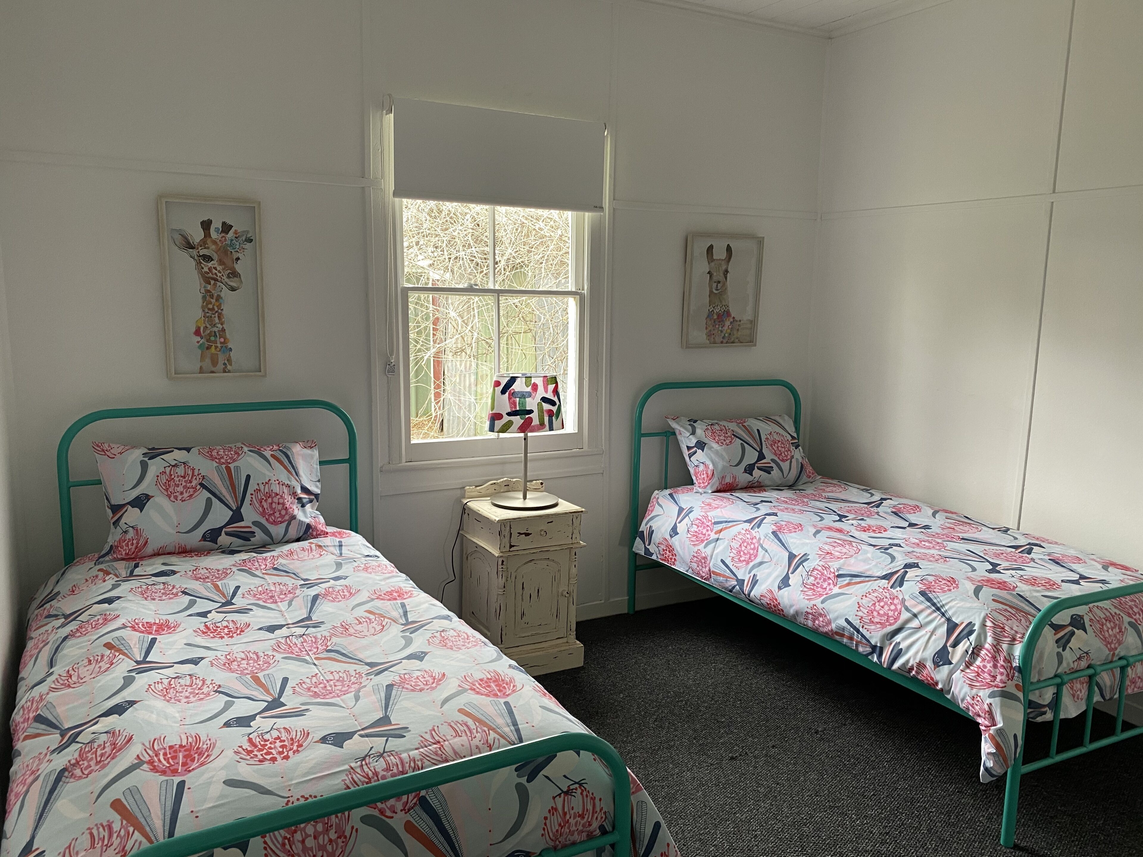 Une chambre avec deux lits simples, une fenêtre et deux tableaux accrochés au mur.