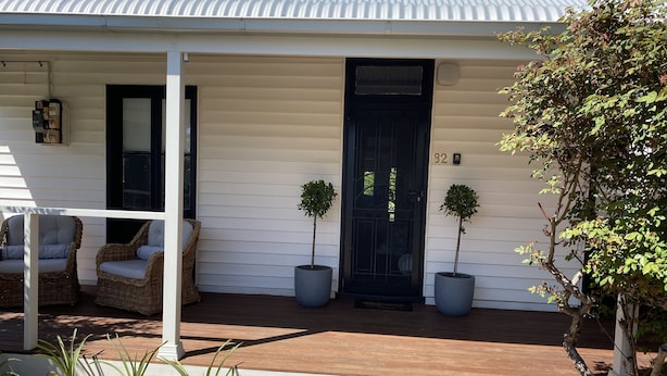 A house with a porch, two potted plants, and two wicker chairs.
