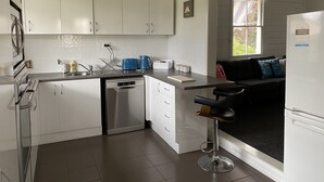 A modern kitchen with white cabinets, a dishwasher, a coffee maker, and a bar stool.