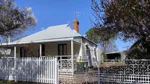 A single-story house with a white picket fence, a chimney, and a metal gate.