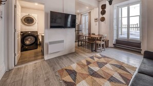 A modern living room with a flat-screen TV, a dining area, and a laundry room. - 2-Bed River View | Private Terrace+Sauna (Quebec City)