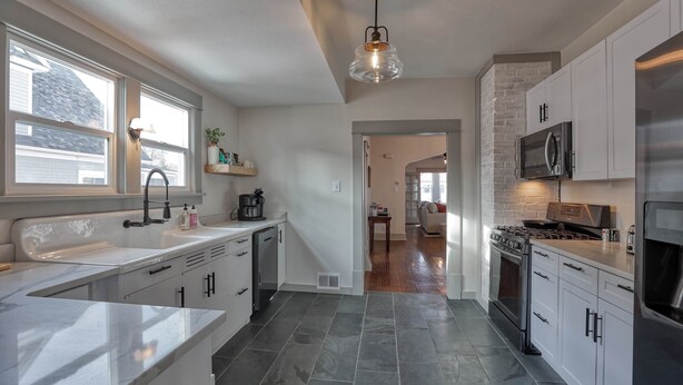 A modern kitchen with white cabinets, a stainless steel refrigerator, a built-in oven, and a large window. - Circle Bar Manor — Spacious 4BR, Sheridan WY (Sheridan)