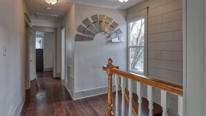 A hallway with wooden flooring, a white railing, and a ceiling light fixture. - Circle Bar Manor — Spacious 4BR, Sheridan WY (Sheridan)