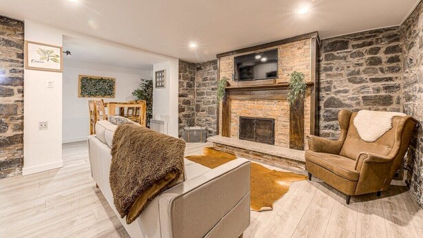 A cozy living room with a stone wall, a fireplace, a sofa, and a leather chair. - Modern Meets Rustic- 2 Bedroom in Old Quebec (Québec)