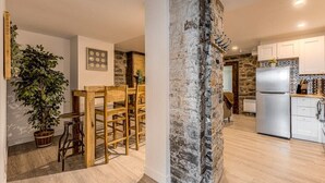 A modern kitchen with a stone accent wall, wooden dining area, and a large refrigerator. - Modern Meets Rustic- 2 Bedroom in Old Quebec (Québec)