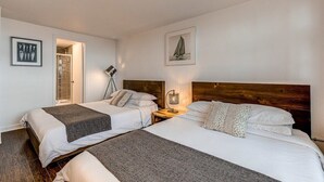 A hotel room with two beds, a wooden headboard, a framed picture of a sailboat, and a floor lamp. - Modern Meets Rustic- 2 Bedroom in Old Quebec (Québec)