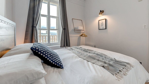 Een slaapkamer met een bed, een raam met gordijnen, een wandlamp en een ingelijste foto.