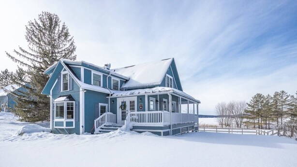 Una casa grande de dos pisos con un porche y un paisaje cubierto de nieve.