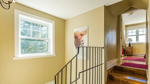 Una escalera con barandilla de metal, un ventanal con vistas a follaje y un cuadro en la pared.