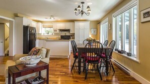 Una cocina amplia con armarios blancos, una zona de comedor con mesa y sillas de madera, y una araña.