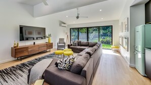 A modern living room with a sectional sofa, a flat-screen TV, a wooden console, and a large window offering a view of the outdoors.