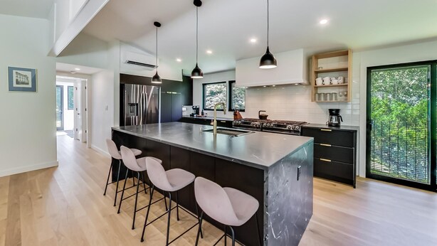 A modern kitchen with a central island, pendant lighting, and a view of greenery outside.