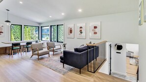 A modern living room with a sofa, chairs, a dining area, and artwork on the walls.