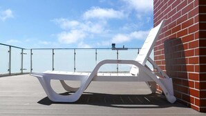 A white lounge chair on a deck with a glass balustrade and a red brick wall. - Seaside Apartment | 400 m to the Beach, Gym, Balcony (Kołobrzeg)