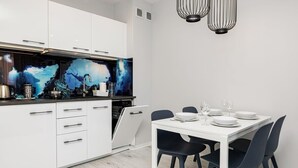 A modern kitchen with white cabinets, a black countertop, and a dining area with a white table and black chairs. - Seaside Apartment | 400 m to the Beach, Gym, Balcony (Kołobrzeg)
