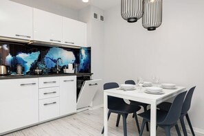 Une cuisine moderne avec des meubles blancs, un plan de travail noir et un coin repas comprenant une table blanche et des chaises noires.
