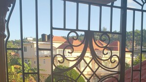 Un balcone con cancello in ferro battuto, pavimento piastrellato e vista su edifici e vegetazione.