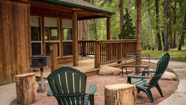 Eine Holzhütte mit einer Terrasse, Sitzgelegenheiten im Freien und einem Grill.