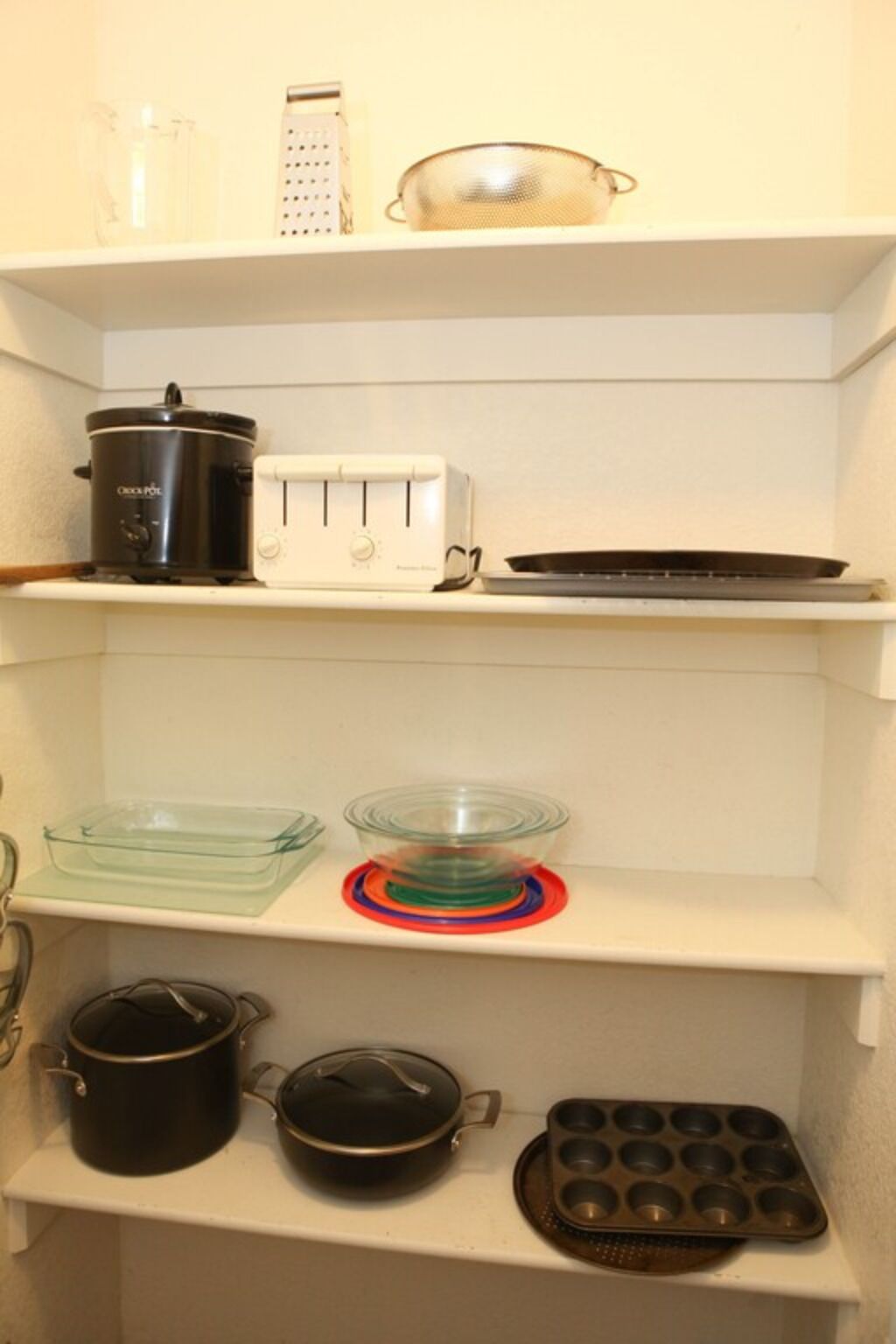 A kitchen with a toaster, a slow cooker, a glass baking dish, a muffin tin, and a pot on the counter.