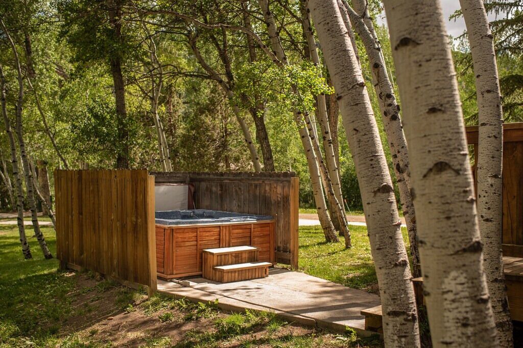 A wooden hot tub structure in a forested area with a wooden deck and steps leading up to it.