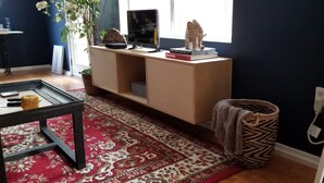 Una sala de estar con pared azul oscuro, un mueble de madera, un televisor y una alfombra roja estampada.
