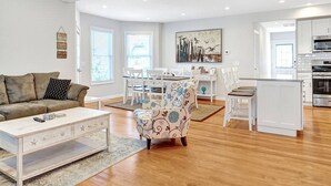 Uma sala de estar espaçosa com piso de madeira, um sofá, uma mesa de centro e um espaço de jantar com cadeiras e uma mesa.