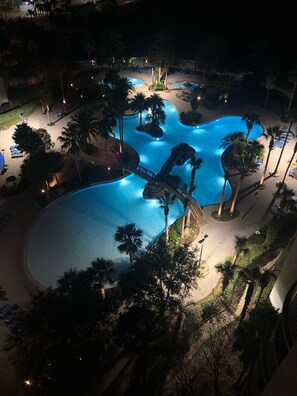 A large outdoor swimming pool with multiple sections, surrounded by palm trees and lounge chairs.