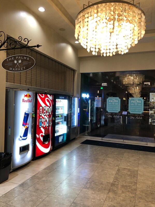 A vending machine area with Red Bull and Coca-Cola machines, a sign for The Palms Market, and a chandelier.