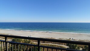 A beach view from a balcony with a railing, clear sky, and calm sea. - Beautiful Clean Modern Direct Oceanfront Unit With Amazing Views (Myrtle Beach)