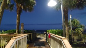 A wooden pathway leading to a beach, flanked by palm trees and a metal railing. - Beautiful Clean Modern Direct Oceanfront Unit With Amazing Views (Myrtle Beach)