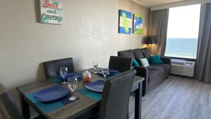 A hotel room with a dining area, a sofa, and a large window with a view of the sea. - Beautiful Clean Modern Direct Oceanfront Unit With Amazing Views (Myrtle Beach)