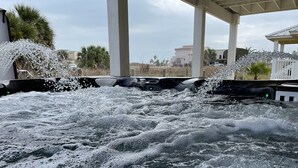 Una vasca idromassaggio con l'acqua che schizza, circondata da un'area coperta con colonne e palme.