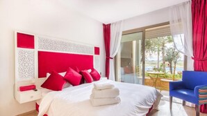 Een hotelkamer met een groot bed, rode en witte decoratie, een blauwe stoel en uitzicht op de omgeving.