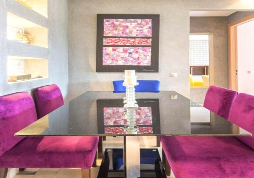 A dining area with a glass table, purple upholstered chairs, and a framed abstract artwork on the wall.