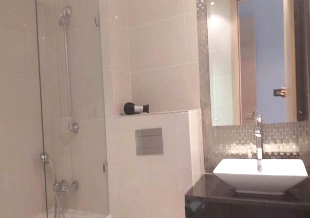 Ein Badezimmer mit einer Duschkabine, einem weißen Waschbecken und einem Spiegel, der eine Person beim Fotografieren zeigt.