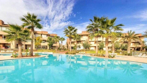 Une piscine entourée de palmiers et de bâtiments d’hôtel.