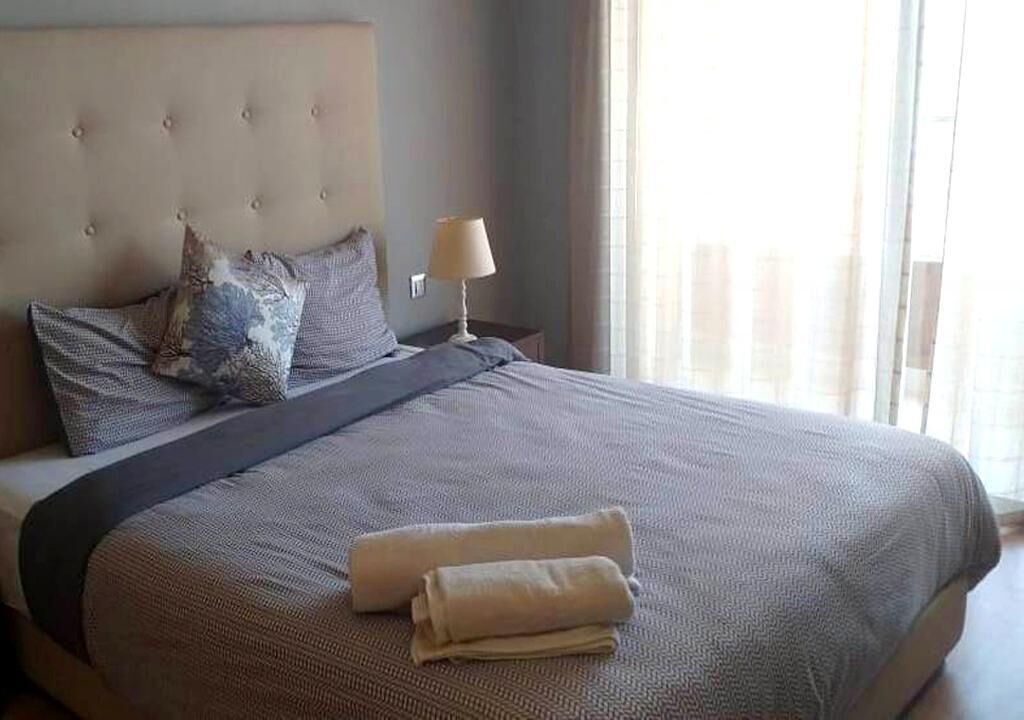 Een keurig opgemaakt bed met een grijze dekbedovertrek, twee kussens en een opgevouwen handdoek.