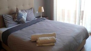 Un lit bien fait, avec une couverture grise, deux oreillers et une serviette pliée posée sur le lit.