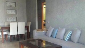 Un salon moderne avec un canapé gris, une table basse en verre et un coin repas avec des chaises blanches.