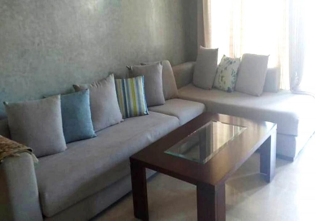 A living room with a sofa, a glass-top coffee table, and a window with curtains.