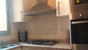 Une cuisine équipée d’une cuisinière à gaz, d’un four en acier inoxydable et de meubles de rangement en bois.