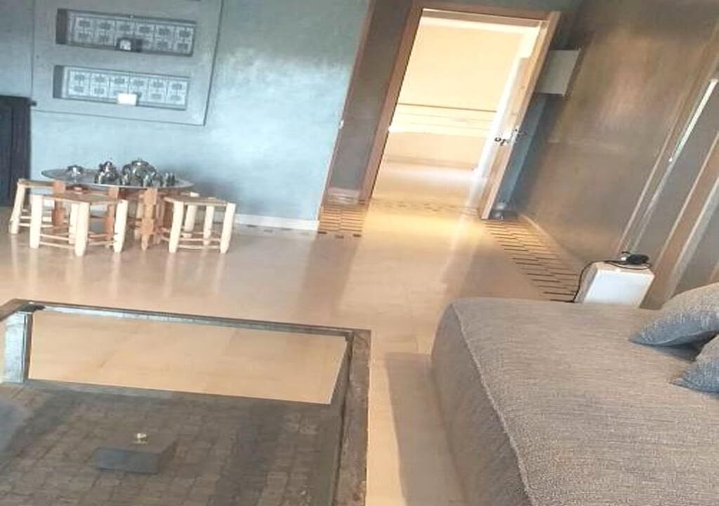 A living room with a sofa, a coffee table, and a dining table with chairs. There is a door leading to another room.